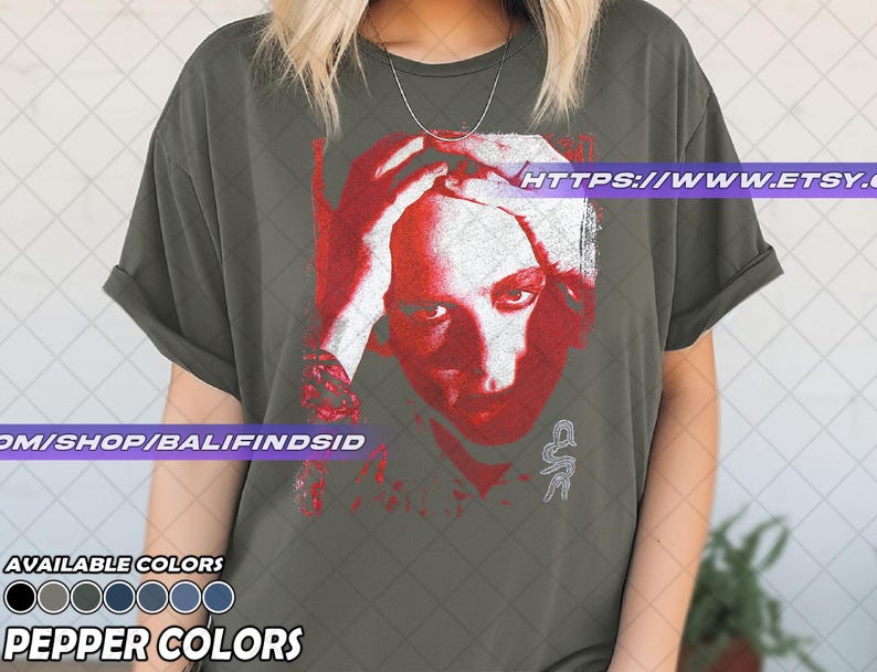 Pu&ograve; includere: T-shirt verde oliva con grafica rossa e bianca di un volto umano con le mani sulla testa. Il testo "HTTPS://WWW.ETSY.COM" &egrave; visibile. Sotto, opzioni di colore e la scritta "PEPPER COLORS".