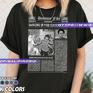 May include: Black t-shirt featuring a newspaper-style graphic with the text "Dominie Fike" and "Dancing in the Court". The graphic includes black and white images and text. The shirt also has a list of available colors.