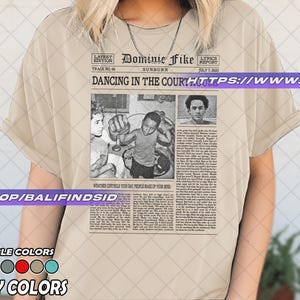 May include: Ivory-colored t-shirt featuring a newspaper-style graphic with the text "Dominie Fike" and "Dancing in the Court." The graphic includes black and white images and text. Available in multiple colors.