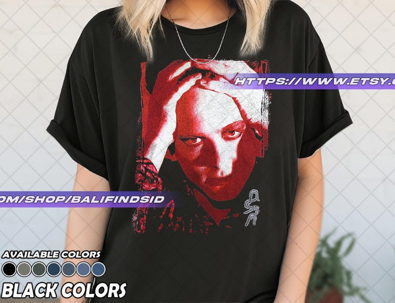 Pu&ograve; includere: T-shirt nero con grafica rossa e bianca di un volto umano, mani sulla testa. La maglietta ha il testo "AVAILABLE COLORS" e "BLACK COLORS" in basso. L'URL del negozio Etsy &egrave; visibile sulla maglietta.