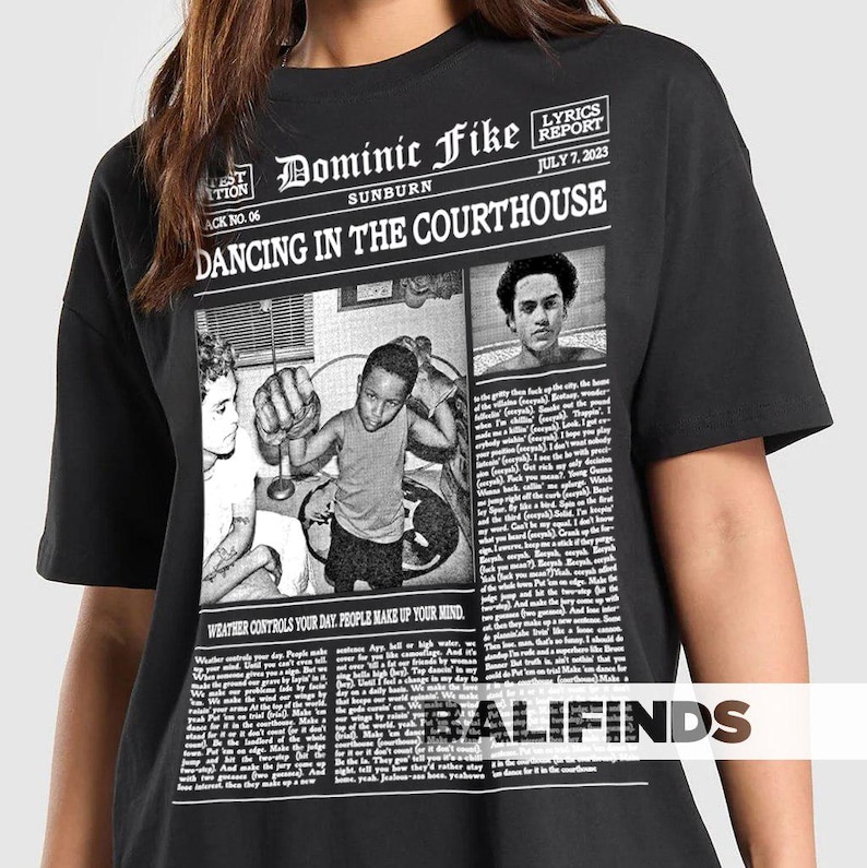May include: Black t-shirt featuring a newspaper-style graphic with the text "Dominic Fike Sunburn Dancing in the Courthouse." The graphic includes images and the text "Lyrics Report July 7, 2023." The shirt also has the text "Weather controls your day. People make up your mind."