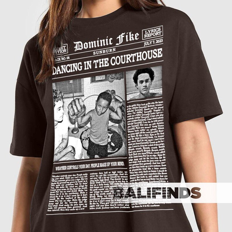 May include: A dark brown t-shirt featuring a newspaper-style graphic with the text "Dominic Fike Sunburn Dancing in the Courthouse." The graphic includes images and text, with the phrase "Weather controls your day. People make up your mind."