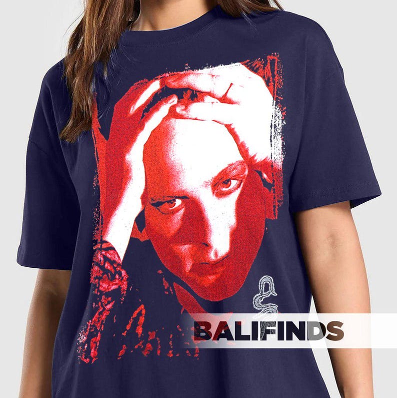 Pu&ograve; includere: T-shirt blu navy con grafica rossa e bianca del volto di una persona, mani sulla testa. La grafica ha un aspetto invecchiato e vintage. Il testo "BALIFINDS" &egrave; stampato in bianco in basso.
