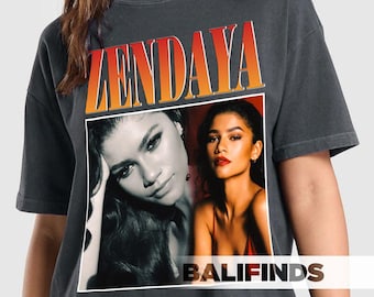 May include: Dark gray t-shirt featuring the name "ZENDAYA" in orange and white block letters. The shirt has a black and white photo of Zendaya on the front. The word "BALIFINDS" is printed in white at the bottom of the photo.