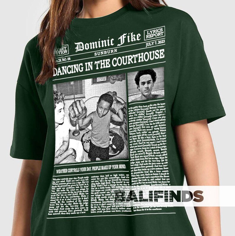 May include: Dark green t-shirt featuring a newspaper-style graphic with the text "Dominic Fike Sunburn Dancing in the Courthouse." The graphic includes images and the text "Weather controls your day. People make up your mind."