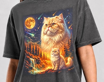 May include: A charcoal gray t-shirt featuring a graphic print of a large, fluffy, golden-orange cat above a smaller cat of the same breed. The scene includes a glowing full moon, falling stars, a forest of pine trees, and a waterfall. The text Pepper Color is printed at the bottom.