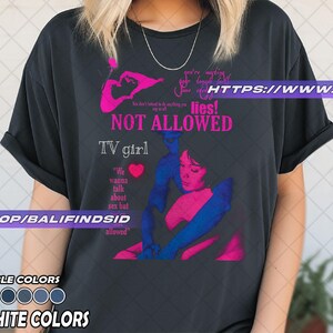 May include: A graphite-colored t-shirt with a graphic design featuring the text "NOT ALLOWED" and "TV girl." The design includes a pink and blue illustration of a person. The shirt also has the text "We wanna talk about sex but allowed."