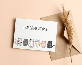 May include: A white card with the text "CON-CAT-ULATIONS!" and a row of six cartoon cats in various colors and patterns. The card is on a light pink background with a brown envelope and a dried grass stalk.