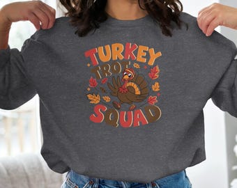 May include: Dark gray sweatshirt with the words "TURKEY TROT SQUAD" in orange and brown. A cartoon turkey with a red wattle and a pilgrim hat is in the center, surrounded by fall leaves.