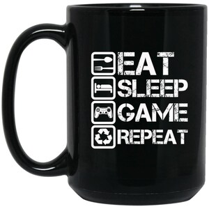 May include: Black ceramic coffee mug with a white graphic that reads "Eat Sleep Game Repeat" with icons for eating, sleeping, gaming, and recycling.