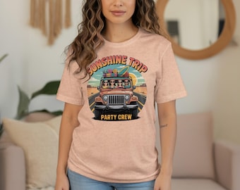 Op de afbeelding: Perzikkleurig T-shirt met een afbeelding van een jeep met passagiers, bagage en een surfplank. De tekst op het shirt luidt "Sunshine Trip Party Crew."