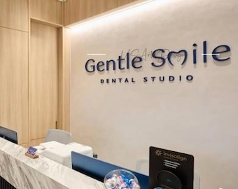 May include: Interior shot of a dental studio reception area. The wall features the words "Gentle Smile Dental Studio" in dark blue lettering. A reception desk with a marble countertop is in the foreground, with a sign for Invisalign.