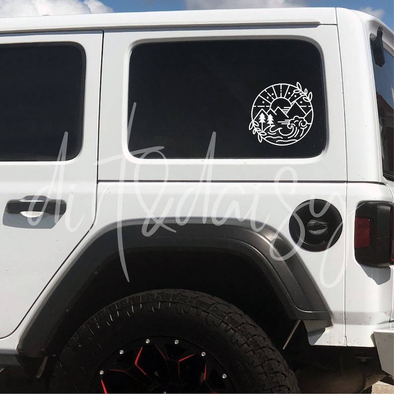 May include: White Jeep with a black and white sticker on the back window. The sticker is a circle with a mountain scene inside. The Jeep has a black tire with a red rim.