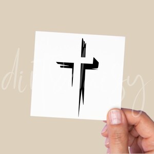 Pu&ograve; includere: Un disegno a croce nera stilizzato su un quadrato bianco. La croce ha un aspetto strutturato, come una pennellata. L'immagine &egrave; tenuta da una mano su uno sfondo neutro. La croce &egrave; un simbolo di fede e cristianesimo.