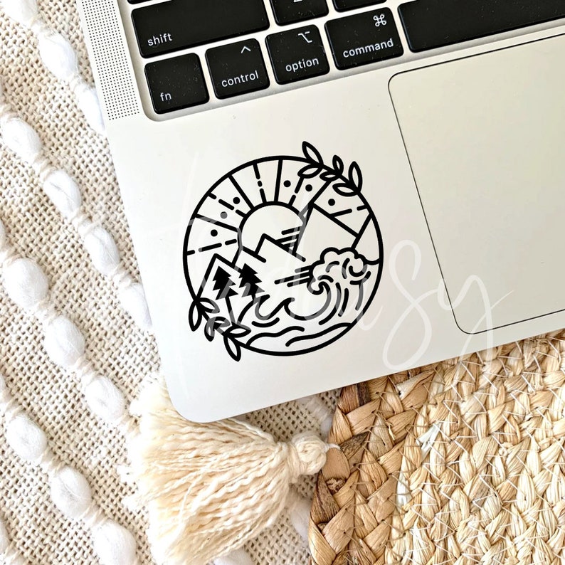May include: Black and white sticker of a sun, mountains, and waves in a circle. The sticker is on a silver laptop.