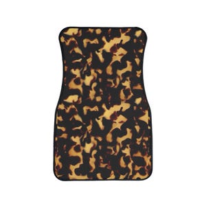 May include: A car floor mat with a tortoiseshell pattern. The mat features a black border and a repeating design of brown and yellow shapes, creating a mottled effect. The mat is rectangular with rounded corners.