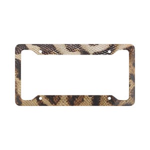 May include: A rectangular license plate frame featuring a brown, tan, and black snakeskin pattern. The frame has four circular mounting holes, one in each corner, and a wide border design that surrounds the central rectangular opening.