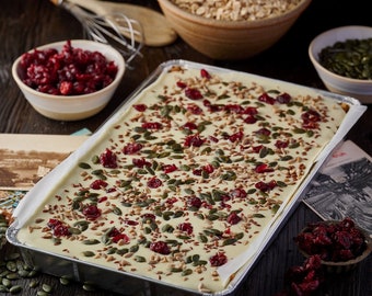 May include: A white chocolate bark topped with cranberries, pumpkin seeds, and sunflower seeds in a silver baking pan.