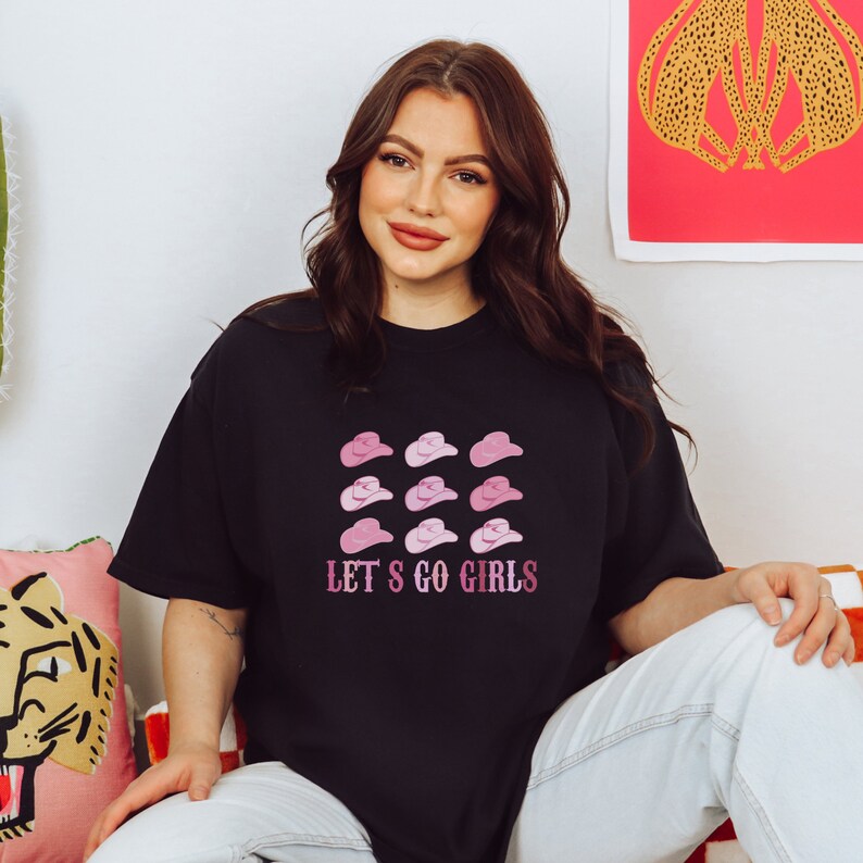 May include: A black t-shirt with a pink and white graphic of cowboy hats and the text "Let's Go Girls".