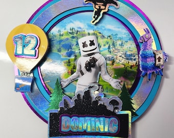 Könnte beinhalten: Ein runder Tortendekor mit Fortnite-Motiv. Es zeigt eine Figur mit einem Marshmallow-Kopf, ein Lama, einen Heißluftballon und einen Fallschirm. Der Tortendekor ist mit schimmerndem Glitzer und dem Namen "Dominic" verziert.