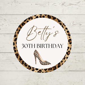 May include: A round sticker with a leopard print border and a cream-colored center. The text "Betty's 30TH BIRTHDAY" is written in elegant brown script. A high-heeled shoe with a leopard print design is featured at the bottom.