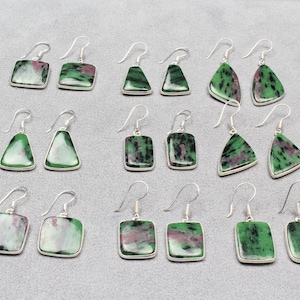 Puede incluir: Un conjunto de 18 pendientes de piedras preciosas verdes y rosas con ganchos de plata. Los pendientes son de varias formas, incluyendo cuadrada, triangular y de lágrima.