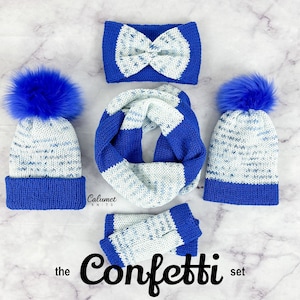 Könnte beinhalten: Ein blaues und weißes Strickmützen-, Schal- und Stirnband-Set mit einem Bommel an jeder Mütze. Das Set heißt "the Confetti set".