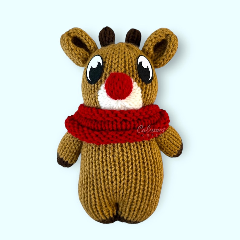 K&ouml;nnte beinhalten: Ein gestricktes Rentier-Spielzeug mit einem roten Schal und einer roten Nase. Das Rentier hat gro&szlig;e braune Augen und ein wei&szlig;es Gesicht.
