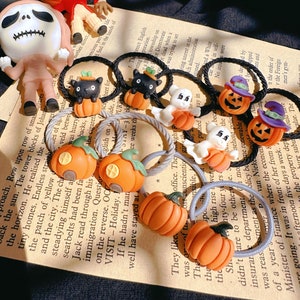 Pode incluir: Uma cole&ccedil;&atilde;o de el&aacute;sticos de cabelo com tema de Halloween. Os el&aacute;sticos apresentam ab&oacute;boras laranja, gatos pretos, fantasmas e jack-o'-lanterns. Os acess&oacute;rios est&atilde;o em um fundo de papel impresso.