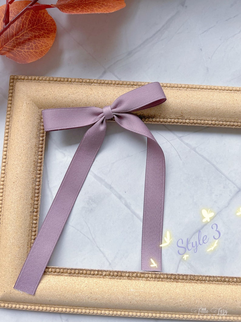 May include: A mauve ribbon bow with long tails sits on a gold picture frame. The text "Style 3" is written in a cursive font with small butterfly illustrations. The background is a marble-effect surface.