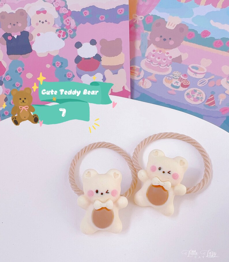 May include: Two cream-colored teddy bear hair ties with brown accents and pink cheeks. The bears are attached to beige elastic bands. The background features illustrations of teddy bears and the text "Cute Teddy Bear".