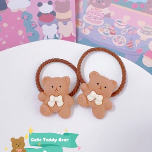May include: Two brown teddy bear hair ties with white bows. The hair ties have a brown, twisted rope design. The image also includes a graphic that says "Cute Teddy Bear" and the number "3".
