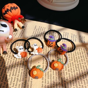 Pode incluir: Uma cole&ccedil;&atilde;o de el&aacute;sticos de cabelo com tema de Halloween. Os el&aacute;sticos apresentam ab&oacute;boras laranjas, fantasmas e jack-o'-lanterns. Alguns t&ecirc;m chap&eacute;us de bruxa. O fundo &eacute; um papel impresso.