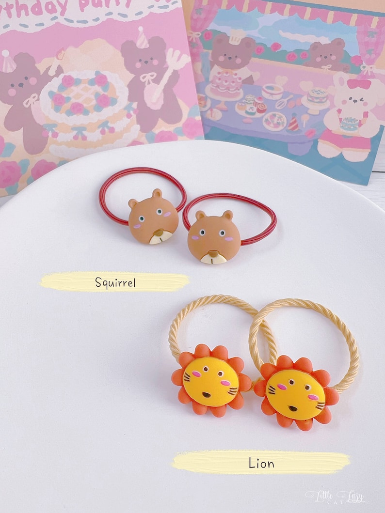 May include: Two sets of hair ties with animal designs. One set features brown squirrel faces on red bands, and the other has yellow lion faces with orange manes on tan bands. The word "Squirrel" and "Lion" are written below each set.