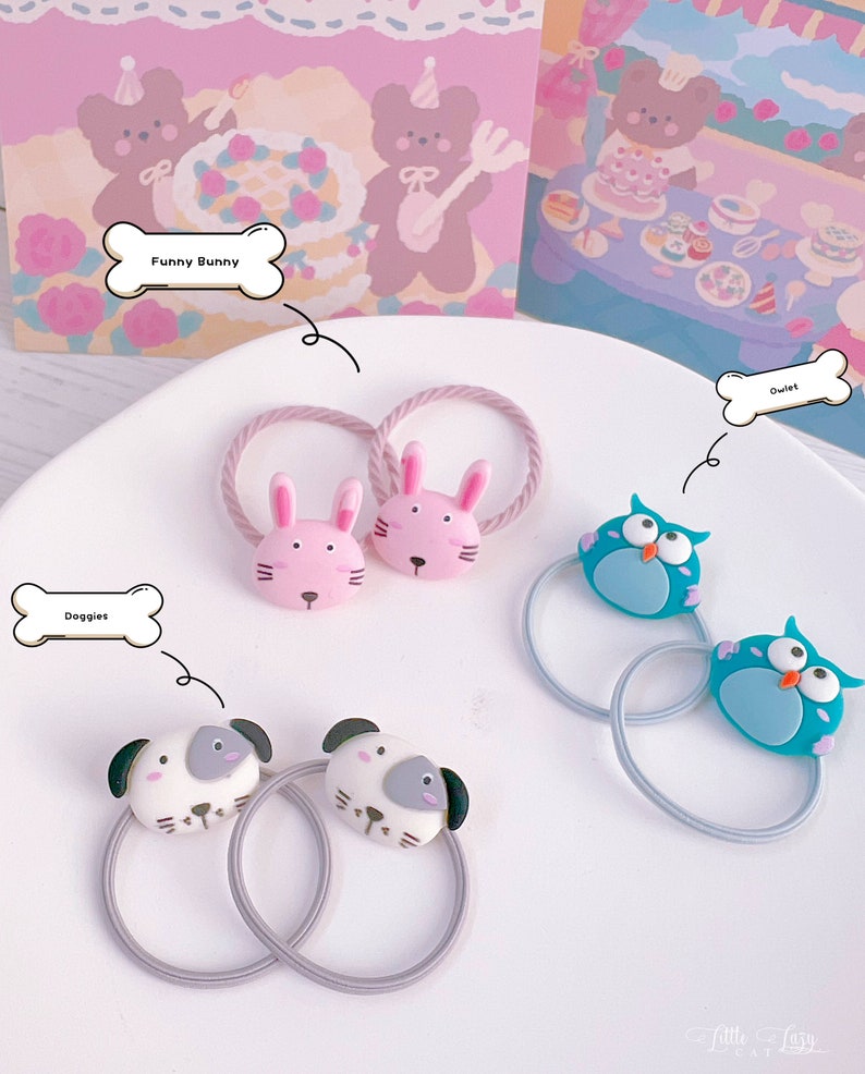 May include: A collection of hair ties with animal-themed designs. The ties feature pink bunny, blue owl, and white dog faces. The hair ties are on a white plate with a pink and white background. The text on the image says "Funny Bunny", "Owlet", and "Doggies".