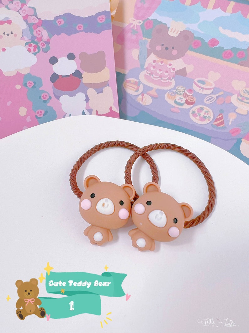 May include: Two brown teddy bear hair ties with pink cheeks and white accents. The hair ties have a brown rope-like texture. The image also includes a teal banner with the text "Cute Teddy Bear" and the number "1".
