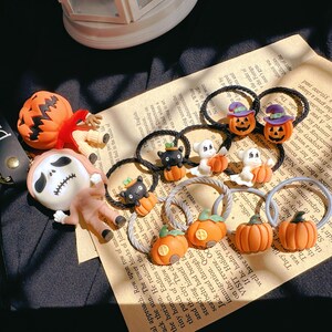 Pode incluir: Acess&oacute;rios de cabelo com tema de Halloween, com desenhos de ab&oacute;boras, fantasmas e gatos pretos. Os enfeites s&atilde;o presos a el&aacute;sticos pretos, sobre um fundo de papel vintage.