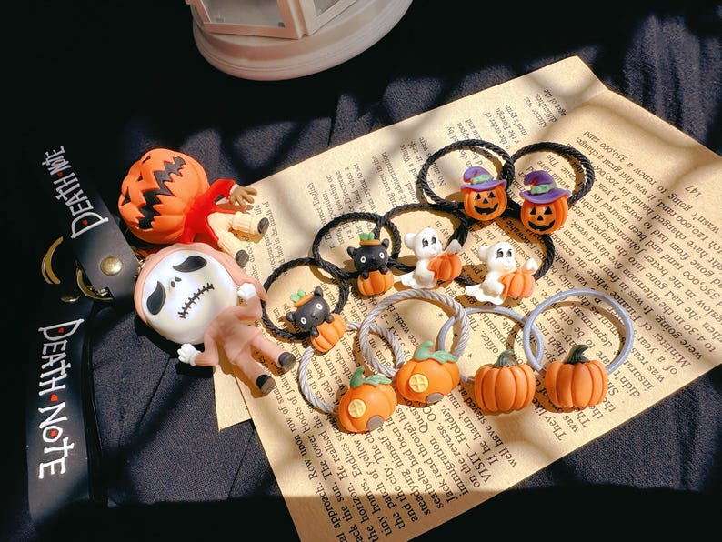 Pode incluir: Acess&oacute;rios de cabelo com tema de Halloween, com desenhos de ab&oacute;boras, fantasmas e gatos pretos. Os enfeites s&atilde;o presos a el&aacute;sticos pretos, sobre um fundo de papel vintage.
