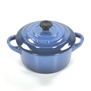 Może przedstawiać: Niebieski emaliowany żeliwny garnek Le Creuset z pokrywką i dwoma uchwytami. Pokrywka ma czarny uchwyt, a nazwa marki jest wytłoczona z boku. Idealny do gotowania.