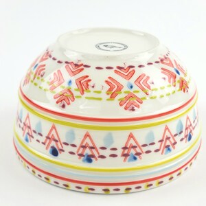 May include: White ceramic bowl with a colourful geometric pattern. The pattern features red, yellow, blue, and green colours. The bowl is perfect for serving snacks, salads, or desserts.