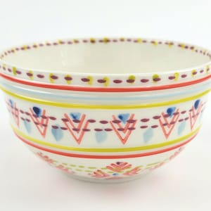 May include: A white ceramic bowl with a colourful geometric pattern. The pattern features red, yellow, blue, and purple accents. The bowl is ideal for serving snacks, salads, or desserts.