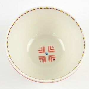 May include: White ceramic bowl with a red and yellow geometric design around the rim and a red and blue geometric design in the centre.