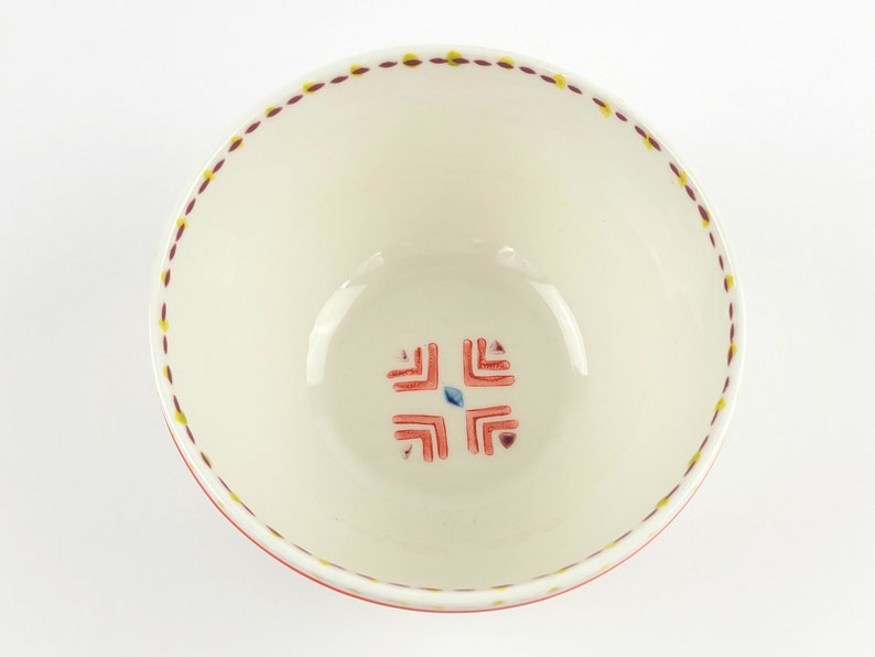 May include: White ceramic bowl with a red and yellow geometric design around the rim and a red and blue geometric design in the centre.