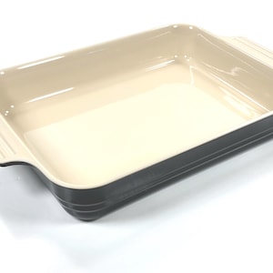 May include: A rectangular baking dish with a cream-colored interior and a dark charcoal gray exterior. The dish features two integrated handles on the short sides, each with three horizontal ridges, and a smooth, glossy finish throughout.