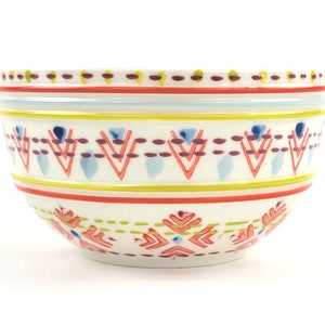 May include: A white ceramic bowl with a colourful geometric pattern. The pattern features red, yellow, blue, and purple accents. The bowl is ideal for serving snacks, salads, or desserts.