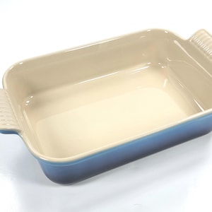Op de afbeelding: Een rechthoekige bakvorm met een crèmekleurige binnenkant en een blauwe buitenkant. De vorm heeft twee handvatten. Geschikt voor ovenschotels en desserts. Afmetingen: ongeveer 25 cm lang en 18 cm breed.