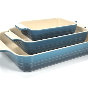 May include: Three rectangular baking dishes in graduated sizes, stacked together. The dishes have a blue gradient exterior and off-white interiors and handles. The largest dish is about 30 cm long.