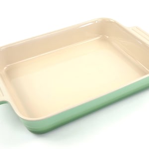 May include: A rectangular baking dish with a light green exterior and a cream-colored interior. The dish has two handles and is made of ceramic. This kitchenware is perfect for baking casseroles and desserts.