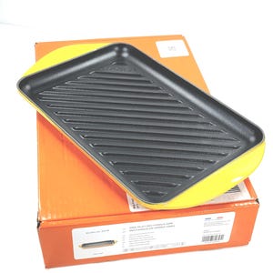 Puede incluir: Una plancha rectangular amarilla y negra con una superficie de cocción acanalada. La plancha está encima de una caja naranja. La caja tiene texto, incluidas las dimensiones de la plancha, que son 32 cm.
