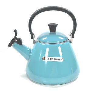 May include: A turquoise Le Creuset kettle with a black handle and spout lever. The kettle has a rounded body and a black knob on the lid. The Le Creuset logo is visible on the front. This kettle is designed for stovetop use.